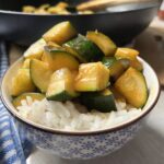 stir fry zucchini on a bed of white rice in a blue and white bowl
