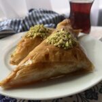 Baklava pockets on a white plate with a glass of Turkish Chai and blue tea towel