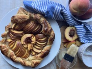 Peach galette on a white serving plate with blue and white tea towel