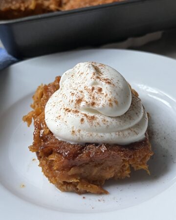 square piece of sweet potato pone topped with whipped cream on a white plate
