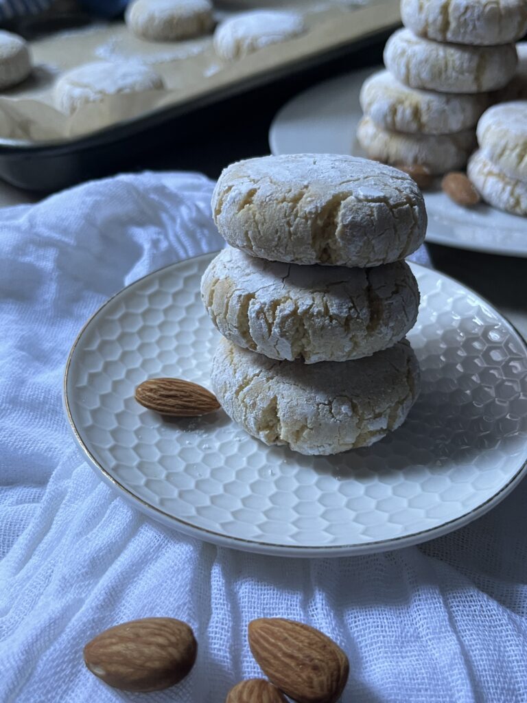 a stack of 3 amaretti (Italian almond cookies) on a plate with more cookies in the background