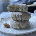 three amaretti stacked up on a small white plate with almonds in the background