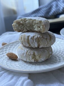 three amaretti stacked up on a small white plate with almonds in the background