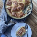 Skillet chicken pot pie with a grey towel on the handle and a serving on a white plate with a fork.